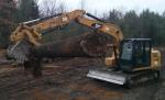 An excavator loading lumber onto a tractor trailer // Une excavatrice chargeant du bois à bord d’un camion gros porteur