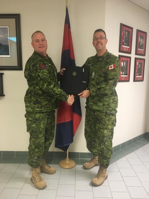 Official handover from the outgoing RCE SM, CWO Croucher (Left) to the incoming RCE SM, CWO Dominic Gaudreau. Of particular note is the awesome circa 1987 Cbt Engr, old school, field cap hat badge that is permanently affixed to the “Succession Planning Binder.”   Photo Credit: MCpl Marc Laliberte.
