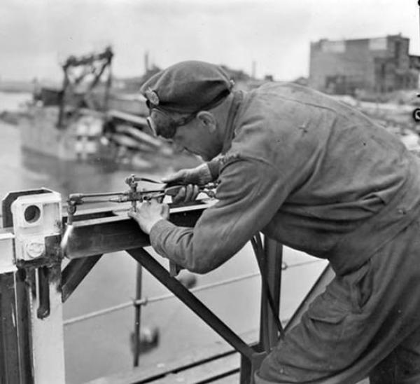 Spr. M.G. Ougler, Second Battalion Canadian Engineers, putting the finishing touches to one of the two new bridges built by the Canadian Engineers. 28 May 1945 / Zutphen, Netherlands. Credit: Canada. Dept. of National Defence/Library and Archives Canada /PA-135997