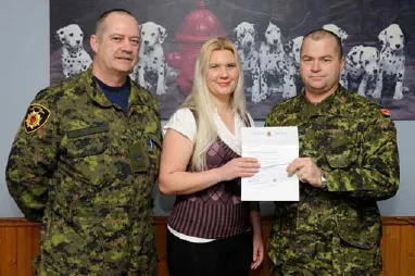 Mrs Nova Fox, wife of Cpl M.R. Fox (Bagotville), receiving the bursary cheque from WO D. Girouard and Sgt P. Calvé.