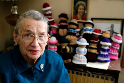 Joan Anstead sits next to a shelf full of Izzy Dolls she knitted for the national project at her home near Roebuck on Thursday. (DARCY CHEEK/The Recorder and Times)