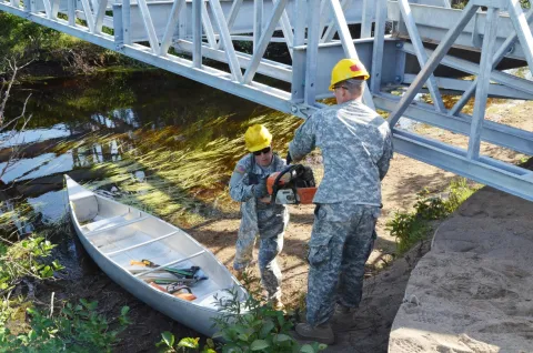 Soldiers with the 652nd Engineer Company from Hammond, WI, load a canoe to transport tools across the river where they are clearing brush and completing a bridge project. PHOTO: Sgt Crystal L. Milton // Soldats de la 652nd Engineer Company de Hammond, WI, chargent un canot pour transporter des outils de l’autre côté de la rivière, où ils doivent dégager les broussailles pour terminer la construction du pont dans le cadre de leur entraînement annuel. PHOTO: Sergeant Crystal L. Milton