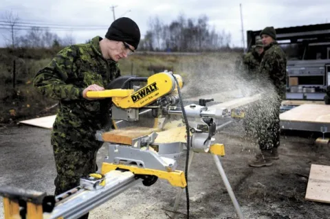 Aviator Joshua McKay of 143 Construction Engineer Flight in Bridgewater N.S. and Private Mitchell Griffith use a chop saw to cut up a board in the military compound created just outside Bathurst, N.B. during Ex NIHILO SAPPER.  Photo: WO Jerry Kean/5 Cdn Div HQ Public Affairs